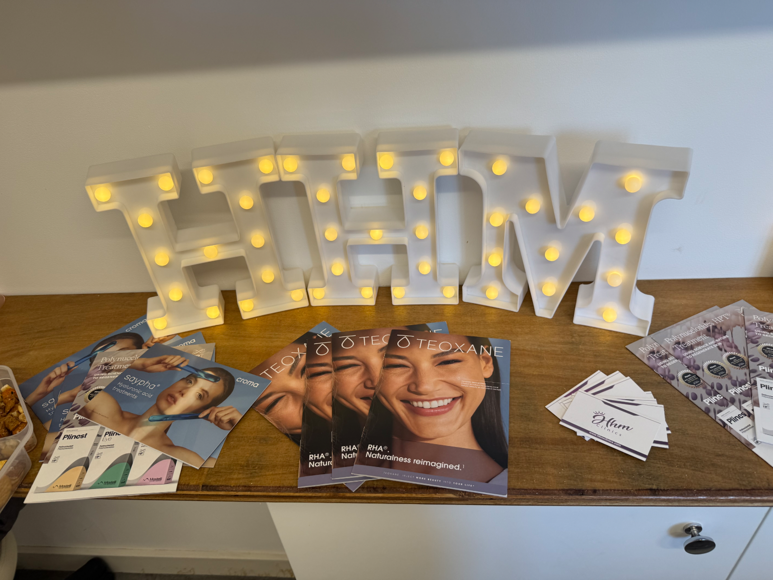 The HHM marquee letters lit on the studio console, surrounded by Teoxane, Croma and Plinest treatment brochures